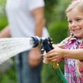 Kind mit Gartenschlauch wässert den Garten